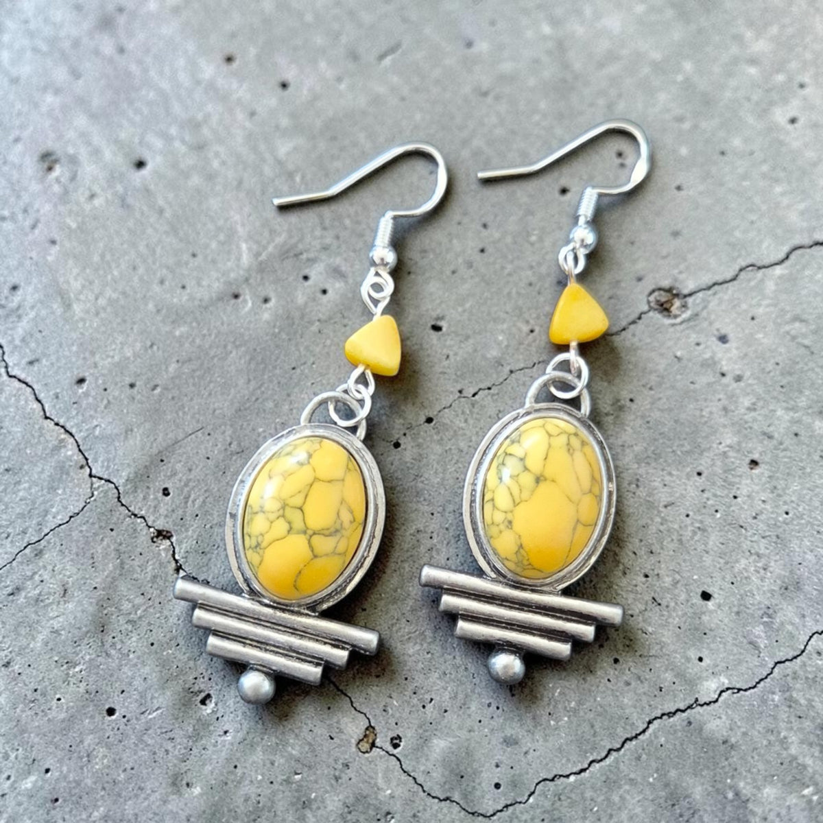 Fury Jewelry & Design yellow turquoise oval drop earrings with silver-tone geometric accents on a grey stone surface.