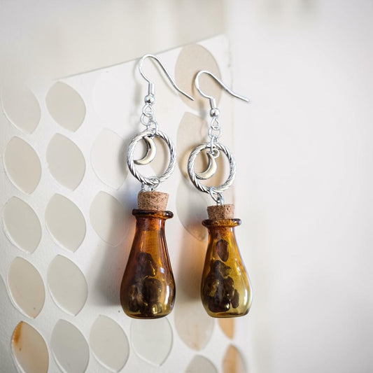 Fury Jewelry & Design amber glass potion bottle drop earrings with silver crescent moon charms and cork stoppers.