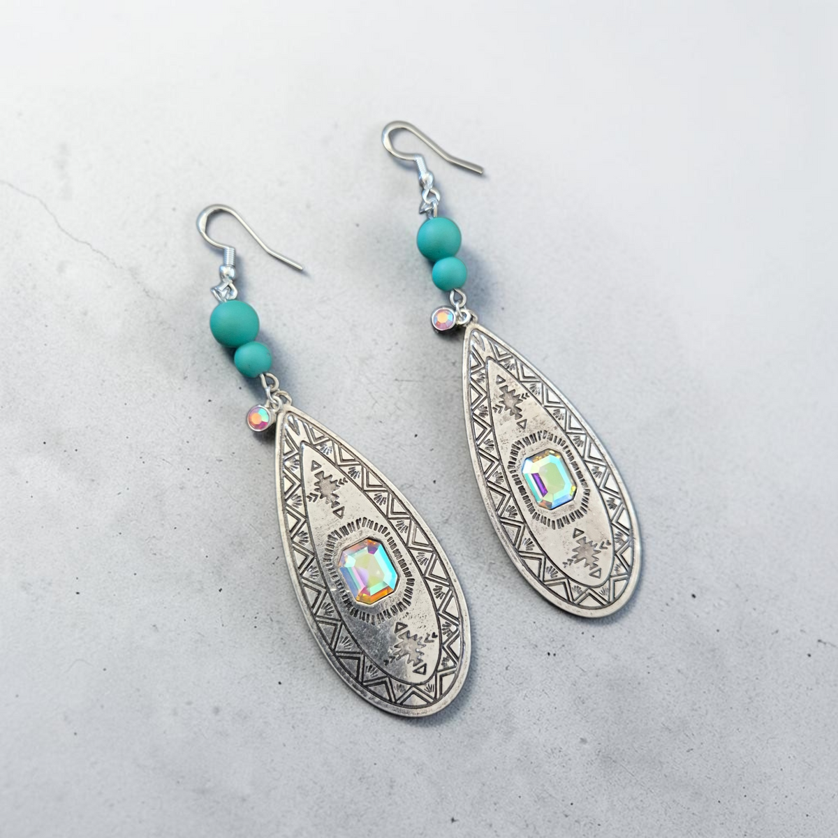 Fury Jewelry & Design teardrop earrings with silver-tone engraving, iridescent crystals, and matte turquoise beads.